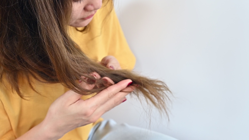 Young Asian woman unhappy with split ends of her hair. Split ends happen when the ends of your hair become dry, brittle, and frayed. | Shutterstock HD Video #1090851093
