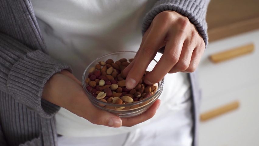 The girl takes peanuts with her hand the girl standing eats peeled peanuts young white girl picks up nuts with her fingers and puts them in her mouth plate of peanuts in the hands of white Asian girl
 Royalty-Free Stock Footage #1090857787
