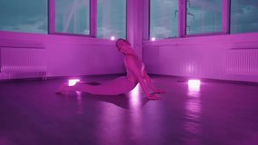 Smiling young girl doing yoga cobra pose at training in fitness room with lilac neon light. The concept of harmony and balance