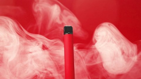 Rotation of one disposable red e-cigarettes, and vapes in with smoke. Concept of bad habits, modern smoking electronic cigarettes.