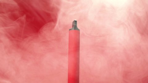 Rotation of one disposable red e-cigarettes, and vapes in with smoke. Concept of bad habits, modern smoking electronic cigarettes.
