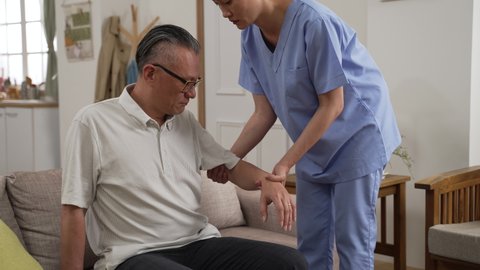 slow motion of Asian elderly man feeling pain from injury while having physical therapy with caregiver’s assistance at home. he says it hurts while the woman is raising his arm