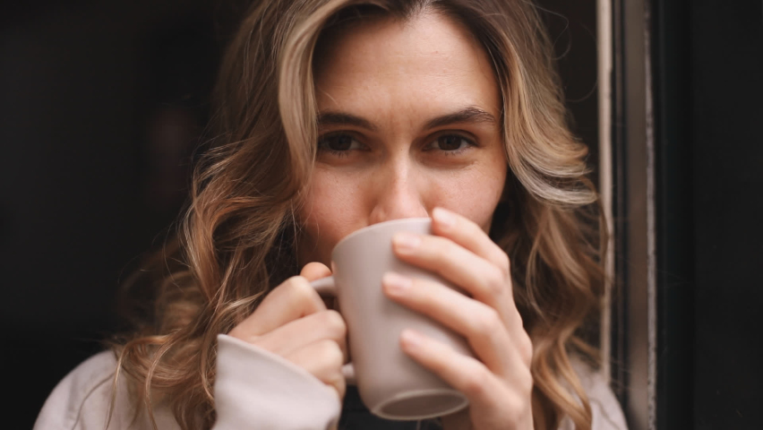 Portrait of joyful young woman enjoying a cup of coffee at home. Smiling pretty girl drinking hot tea. Excited curly blonde woman enjoy. Close up. Royalty-Free Stock Footage #1090860513