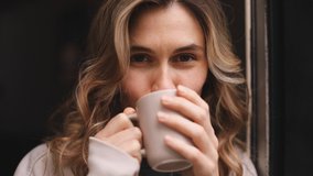 Portrait of joyful young woman enjoying a cup of coffee at home. Smiling pretty girl drinking hot tea. Excited curly blonde woman enjoy. Close up. - Powered by Shutterstock - Get 15% off with code: PIKWIZARD15