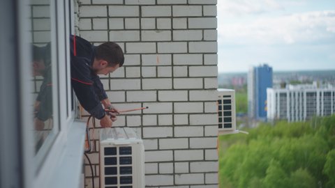 A man at high altitude installs air conditioning. Installation of the external unit of the Air Conditioning System. Summer cooling of the air in the big city