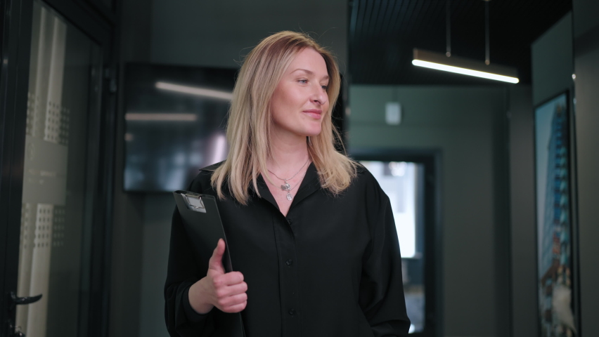 Portrait of a smiling Business woman, a blonde 30-40 years old in a black shirt, walking down the corridor of a business center