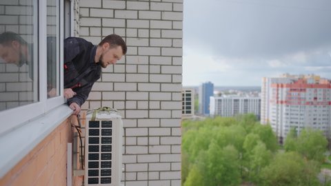 A man at high altitude installs air conditioning. Installation of the external unit of the Air Conditioning System. Creating a microclimate in the apartment