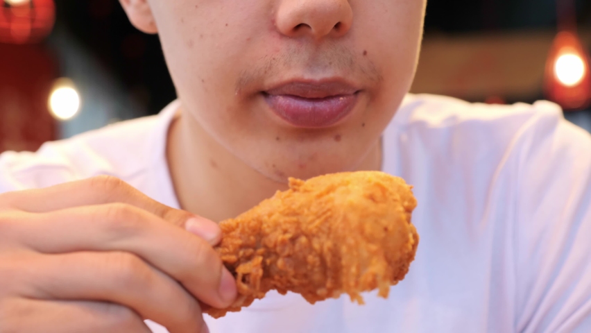 Handsome young man student eating chicken wings, high calorie food, health risks, cholesterol. Close up of male mouth eating junk food indoors. The guy bites a crispy chicken fried in oil. Royalty-Free Stock Footage #1090862925
