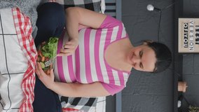 Vertical video. Happy Pregnant Woman Having Healthy Lunch in Bed, Eating Vegetable Salad while Sitting in Lotus Pose. Healthy Food and Nutrition for Expectant Mother