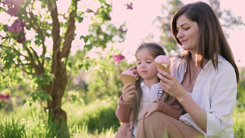 Mom and daughter spend their leisure time in park. Young woman and her four year old daughter are eating ice cream. | Shutterstock HD Video #1090869791