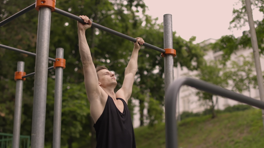 Fitness, sport, exercising, training and lifestyle concept - young man doing pull ups on horizontal bar outdoors. Sporty man working out in outdoor gym in park. | Shutterstock HD Video #1090869925