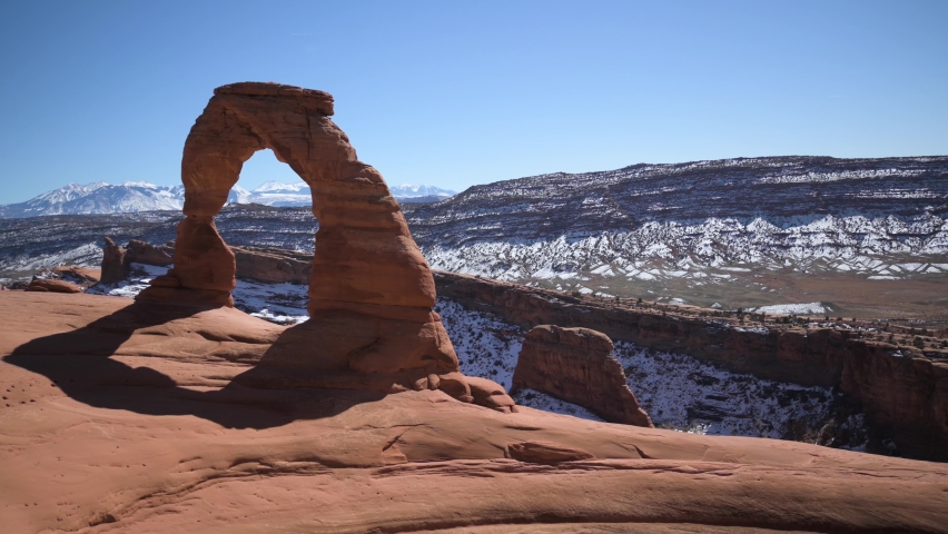 Hiker walking up to and climbing on the Delicate Arch in Arches National Park, pan