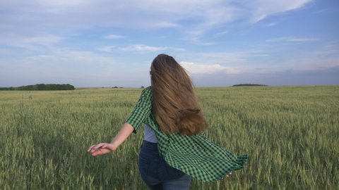 Beautiful teenage girl with long hair in the park. A young girl runs through a wheat field. Happy, free young girl in green wheat. Hair develops in the wind.
