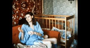 Mother feeds baby with spoon in home room. Young, beautiful woman begs her child to eat in Soviet apartment interior. Happy parents care about child. Vintage color film. Family archive. Retro 1980s