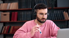 Smart male student listening internet webinar talking online video call making notes working library desk. Clever smiling Hispanic man in headphones distance education e learning training web courses