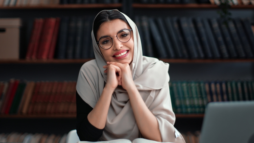 Portrait smiling Muslim woman business student teacher science in hijab posing at library desk laptop workplace. Happy Asian female in eyeglasses prepare exam lecture at college university with book - Powered by Shutterstock - Get 15% off with code: PIKWIZARD15