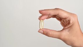 Hand of young woman, girl holds golden capsule with Omega 3 on light background. Vitamins, pills, vitamin d, Supplements, pharmaceutical theme, healthy lifestyle, medicine. Fish oil pill