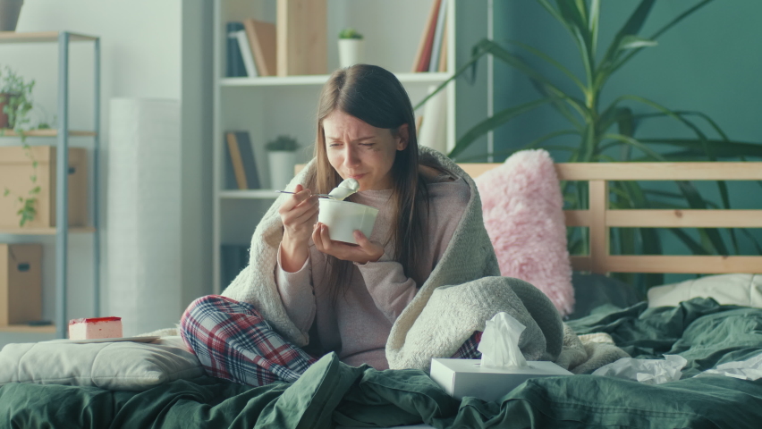 Heartbroken Girl Sitting on Sofa, Crying, Using Tissues, Eating Ice Cream and Holding Phone. Upset Young Woman Wrapped in Blanket Worry Separation or Divorce. Atmosphere of Depression. | Shutterstock HD Video #1090879001