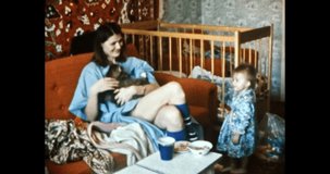 Young mother with pet, small child play in home room. Happy, smiling woman holding cat in arms. Shows an animal to baby girl. Family life indoors. Vintage color film. Family archive. Retro 1980s. 4k