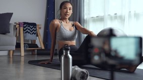 Asian woman using phone camera for live streaming teach yoga online in living room. young female in sportswear exercising at home, watching online fitness classroom.