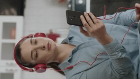 Happy woman dancing to the music she is listening to with headphones connected to her mobile phone in her peaceful home.Woman sitting on sofa using wireless headphones to listen to music at home.