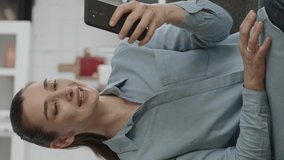 Young woman reading news or text on the phone while drinking coffee at home.The young woman laughs at the message she saw. Slow motion video.Video for the vertical story.