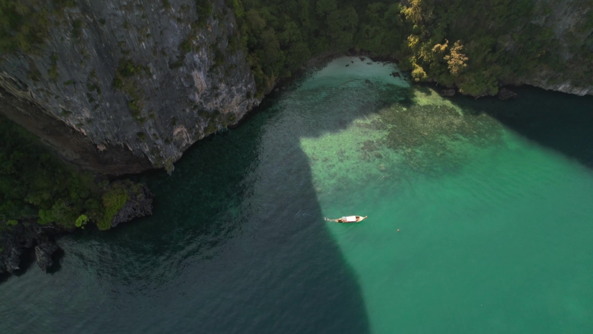 Aerial top down view circling a thai longtail boat on a tour of the islands in Krabi Thailand on a sunny morning through the turquoise blue ocean surrounded by tall limestone mountains | Shutterstock HD Video #1090900521