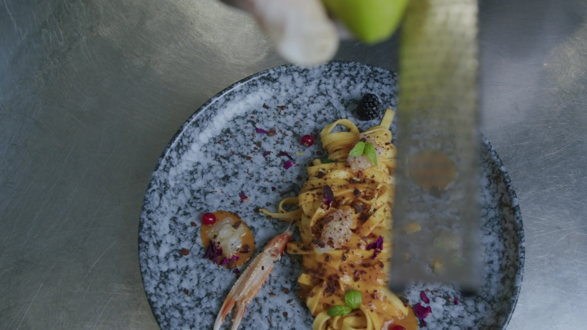 A lemon being grate on a tasty plate of pasta and scampi in Italy by a professional chef in his kitchen