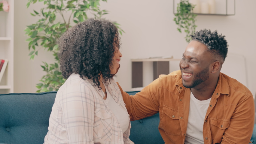 African American couple laughing happily and talking while sitting on couch Royalty-Free Stock Footage #1090903801