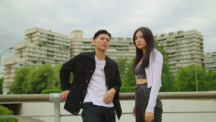 Attractive serious Asian couple looking at camera against multistory buildings dormitory area. Boy and girl wearing casual clother. Teenager love concept Royalty-Free Stock Footage #1090904851