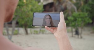 Happy romantic sweet young caucasian couple video call from the beach and showing an amazing beautiful seascape to each other laughing and waving into phone camera during summer holiday or vacation.