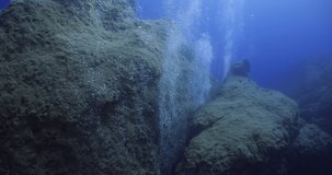  scuba divers exploring around a reef underwater deep blue water big rocks and bubbles ocean scenery