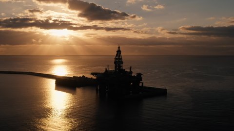 Offshore oil and gas platform aerial view. Silhouette of drilling rig (jack up rig) in sea or ocean at sunrise. Offshore exploration of crude oil and gas. Petroleum and chemical industry concept