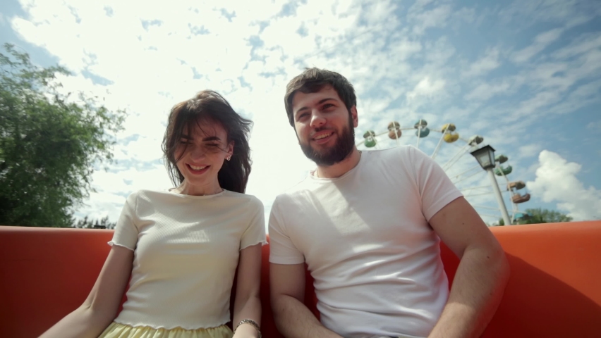 Close up of smiling man with happy woman in amusement park having fun on roller coaster. Selfie of couple in love enjoying extreme roller coaster ride in theme park or amusement park rides