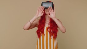 Exited redhead woman using virtual reality futuristic technology VR app headset helmet to play simulation 3D 360 video game, drawing. Ginger girl on beige studio background. People sincere emotions