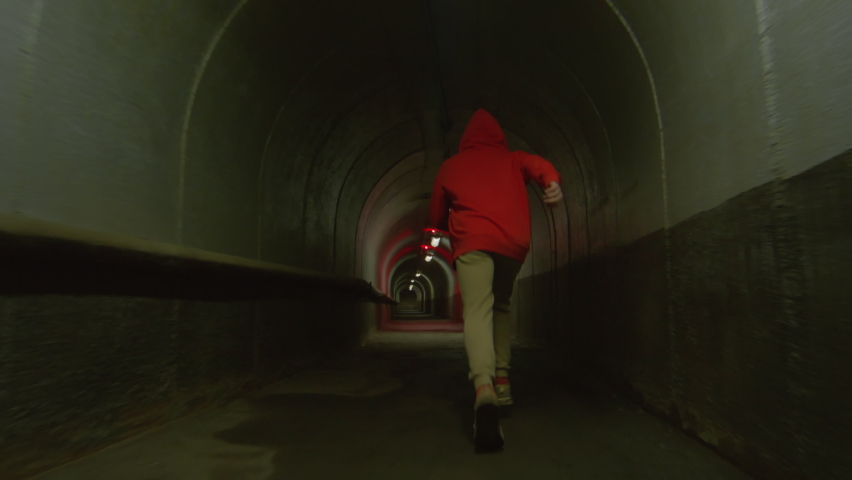 Following shot of parkour athlete running through urban tunnel with red light and performing front flip Royalty-Free Stock Footage #1090910079
