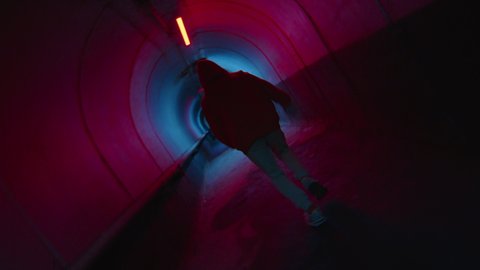 Camera roll of parkour athlete running through dark underground tunnel with neon light and performing side flip Video Stok
