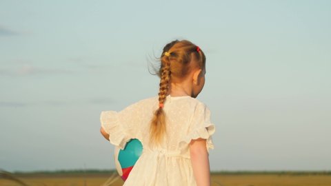 little child girl walks through park with bright colored ball. happy family. concept children dream game. daughter kid plays ball field. child runs with ball along road sunset. happy family concept