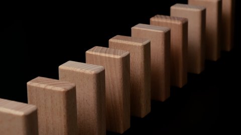 Row of wooden domino falling down against black background. Domino effect.