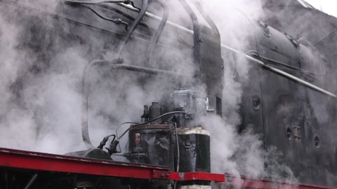 Smoke covering the train. Retro steam locomotive departs from the railway station. Old black steam train much smoke. Vintage locomotive with historical tour. Close-up