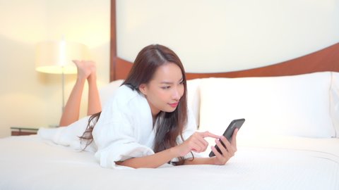 A pretty girl in a hotel robe lies on the bed on her stomach as she texts and then reacts to her successful connection. Title space