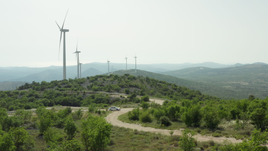 the car goes on the road near the windmills in the mountains. Production of clean environmental energy in nature and people go on a journey. Royalty-Free Stock Footage #1090922313