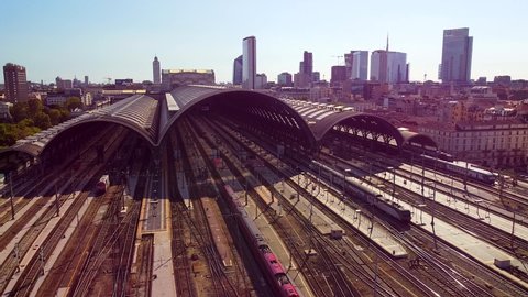 Aerial view of the station. Trains arrive at the station. An old wide arched structure of metal and glass above the station pillars. Tourism. Skyline with tall buildings. Italy, Milan, June 2022