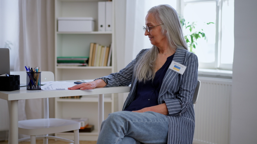 Happy senior woman working as volunteer helping Ukrainians at immigration office, lookin at camera.