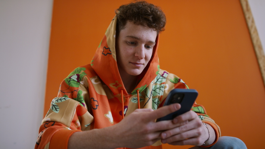 Fashion studio shootingt of a young man in hoodie with smartphone posing over orange background. Royalty-Free Stock Footage #1090923259