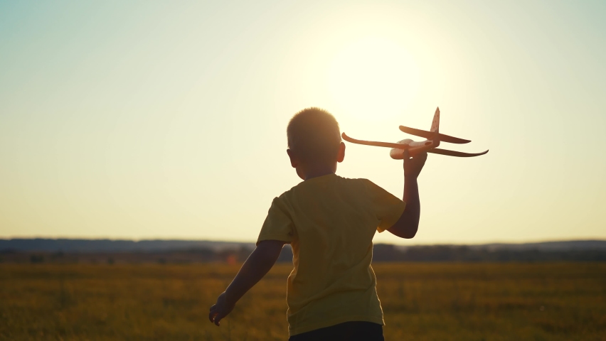 boy run play airplane in the park. happy family kid dream concept. happy boy running across the field in nature in wild park. silhouette kid play airplane running on the grass back view sun
