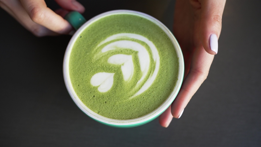 Female hands put cup of green matcha with latte art on black table. Barista serves matcha latte in cafe. Trendy matcha tea in green cup closeup | Shutterstock HD Video #1090927685