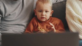 Happy little child watching something on laptop with his parents at home