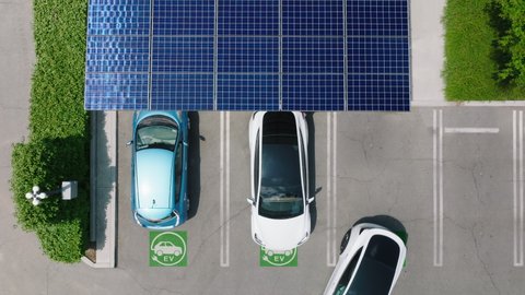 Aerial view of a car parking under solar panels. 4K electric, zero pollution, green energy concept cars at modern city parking lot. Alternative energy for ecological cars under blue solar batteries