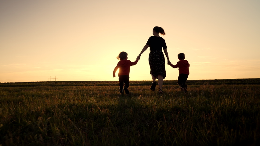 Silhouette of young family - mom and two brothers twins boys runs to the sun on open air field or park, golden hour, flares Happy mother and children, love, freedom, future concept Royalty-Free Stock Footage #1090933291